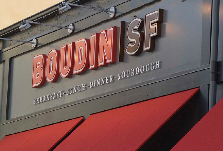 A black shop facade with red awnings and a sign that reads Boudin SF, breakfast, lunch, dinner, sourdough.