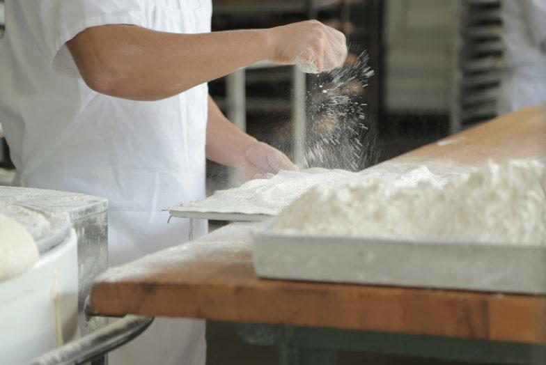 Baker sprinkling flour on table